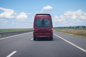 A burgundy minibus rides along a country road. Cargo transportation, transportation of people