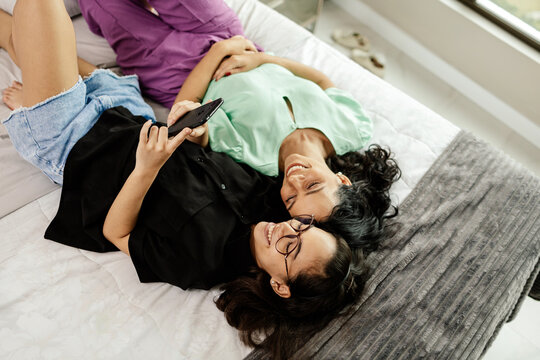 Mother and teenage daughter using smartphone together lying in bed at home. Latina mother and daughter looking at phone watching social media videos while relaxing in bedroom. family and technology