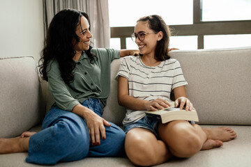 A mother and her teenage daughter laughing happily on the sofa after a satisfying read, the girl...