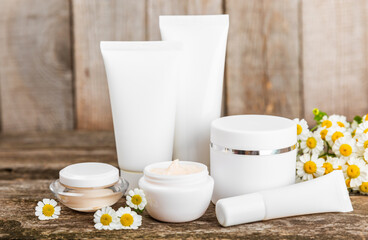 Body and hand cream with chamomile flower on a brown wooden background. Herbal dermatological cosmetic hygiene cream. Natural cosmetic product. Cosmetic tube. Ecological cosmetics.Copy space.