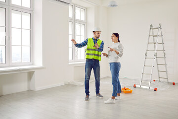 Young woman homeowner discussing design project or repair of new apartment with foreman standing in empty white room. Meeting with builder about interior decoration or home layout. Moving concept.