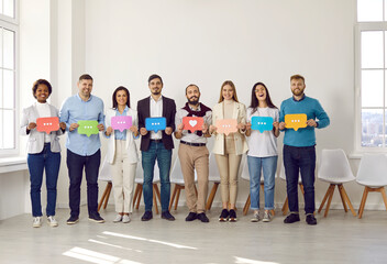 Positive cheerful people stand together in row with symbols of social networks in their hands. People holding speech bubble with mobile messenger chat icons in form of three dots and heart.