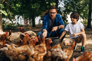A Caucasian man is feeding chickens with his son.