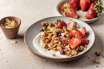 Healthy breakfast: fresh granola, muesli with yogurt, strawberry and honey on beige textured background. Copy space