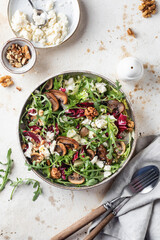 Green salad with feta cheese, arugula, mushrooms, walnut in ceramic bowl on textured background top view. Healthy summer lunch or dinner flat lay with text space