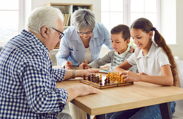 Grandparents and grandchildren playing games at home. Od, retired grandfather and grandmother and little children sitting at table and playing game of chess together. Family, leisure activity concept