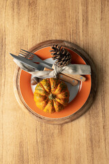 A plate with cutlery is decorated for Thanksgiving with pumpkins and autumn products on a wooden table, top view