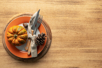 A plate with cutlery is decorated for Thanksgiving with pumpkins and autumn products on a wooden...