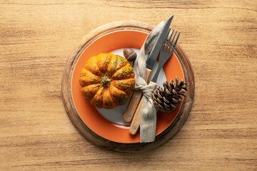 A plate with cutlery is decorated for Thanksgiving with pumpkins and autumn products on a wooden table, top view