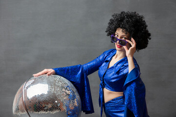 Girl with a disco ball in an afro wig on a gray background. Disco style from the seventies or...