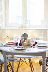 Christmas table setting with burning candles, retro lights and champagne glasses. Warm and cozy atmosphere