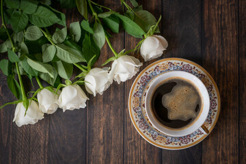 Fototapeta na wymiar Aromatic coffee served in a porcelain cup on a wooden table with a bouquet of white roses