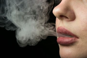 Tobacco smoke comes out of women's lips on a black background