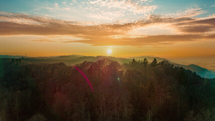 Panorama of a forest in a hilly valley against the backdrop of a setting sun in a cloudy sky
