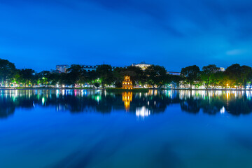 Fototapeta na wymiar Hanoi City Old Quarters Lake at night glowing with vibrant colourful city lights surrounded by old historic buildings small bridge crossing the lake into a temple on a small island Hanoi Vietnam