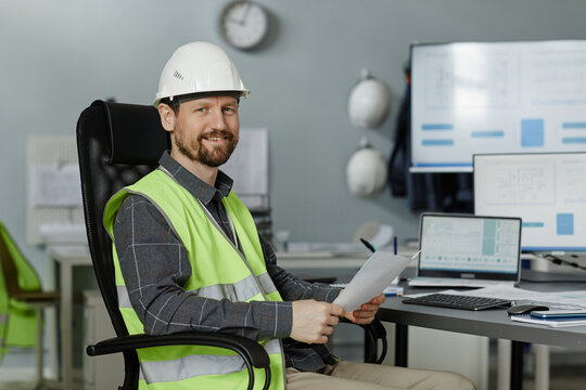 Portrait of smiling engineer wearing hardhat at workplace in office and looking at camera, copy space