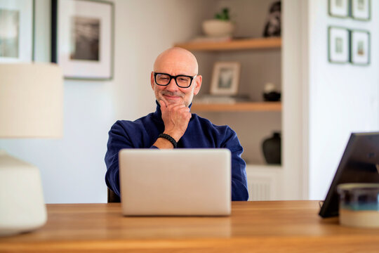 Smiling businessman looking thoughtfully and using laptop at home
