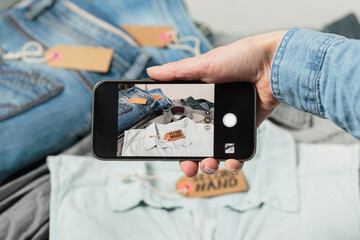 View of womans hand taking photo of denim clothes to upload in second hand fashion app on the...