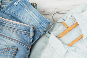 Stack of blue jeans and denim shirt on hanger. Second hand clothing shop. Circular fashion, eco...