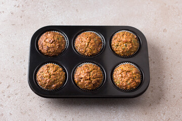 Pumpkin muffins with oatmeal and nuts in a baking dish on a beige textured background. Cooking delicious healthy homemade cakes