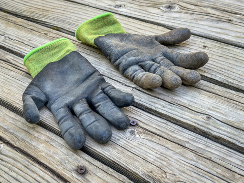 a pair of well used, dirty bamboo garden gloves on a wooden rustic deck