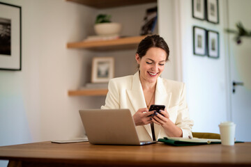 Attractive young woman using mobile phone and laptop and working at home