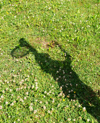 Shadow of a girl playing tennis on the grass in a park.