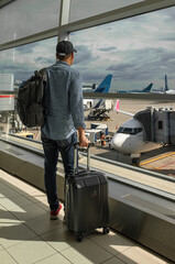 Man With Suitcase in airport looking at aircraft flight through window at Terminal, On His Way To Flight Boarding Gate