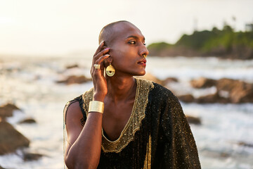 Epatage lgbtq black man poses on scenic ocean beach looks at camera demonstrates jewellery ....