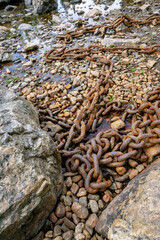A rusty chain is lying on the rocks next to the river. Water touches the chains on a summer day
