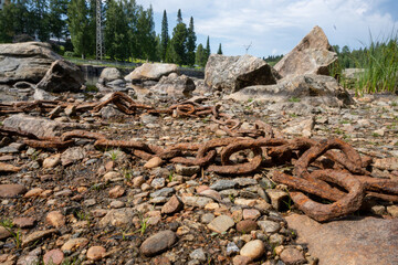 Fototapeta na wymiar A rusty chain is lying on the rocks next to the river. Water touches the chains on a summer day 