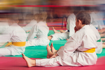 Children's karate group is warming up on the mat in the hall of the sports school.