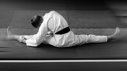 A young karate man is warming up on the tatami in the hall of the sports school with his back to us. Black and white photo with motion blur effect.