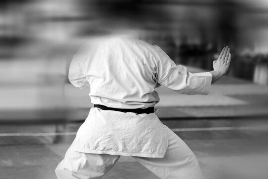 A martial artist in a white kimano with a black master belt demonstrates a technique. Black and white photo with motion blur effect.