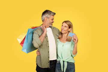 Sales and consumerism concept. Happy middle aged couple showing debit credit card holding shopper bags