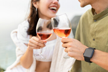 Happy man and woman clanging wine glasses with rose wine, having date and picnic on beach, closeup