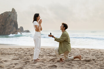Romantic proposal on the seashore. Loving young man with engagement ring making proposal to happy...