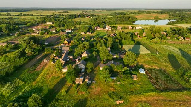 Rural landscape with country houses. Lake in countryside on sunset, aerial view. Green nature at Lake. Drone shot flying over country House in rural. Bird's eye view of agricultural field in rural.