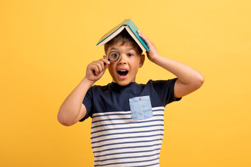 Excited kid cute boy with book on head holding magnifier