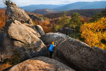 Young tourist hiking between the rocks in the autumn forest. Top view. Wonderful mountain landscape with autumn trees.