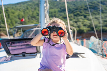 Little girl on a yacht looking through binoculars in the sea