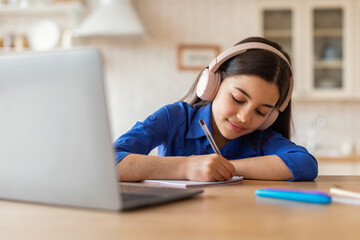 Schooler girl doing homework at laptop taking notes at home