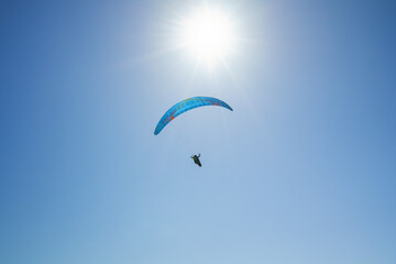 Silhouette of a skydiver with parachute open flying in the air, and bright sun, and blue sky in the background