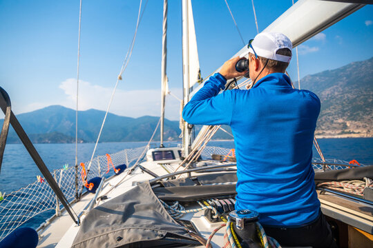Young man captain on the yacht looking through binoculars during sailing boat control. Travel and active life.