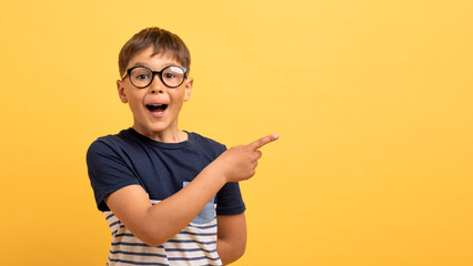 Excited boy in casual t-shirt pointing at copy space