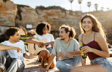 Cheerful millennial african american, asian, european people students with bottles playing guitar, enjoy picnic