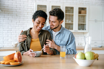 Healthy breakfast. Happy married couple, caucasian man and african american woman, having breakfast at cozy home kitchen with healthy porridge, happy to spend time together at weekend morning, smiling