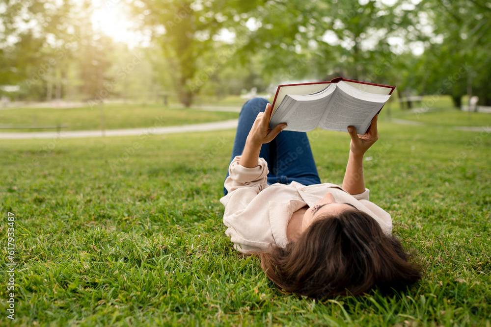 Wall mural student young lady reading book lying on green grass outdoor