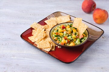 Salsa from fresh cucumber and ripe peach in a ceramic plate on a light wooden background. Served with wheat chips. Mexican cuisine.