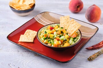Salsa from fresh cucumber and ripe peach in a ceramic plate on a light wooden background. Served with wheat chips. Mexican cuisine.